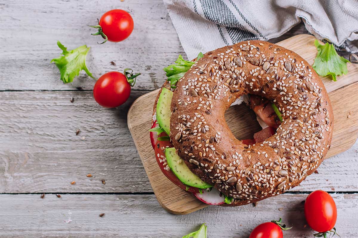 A toasted bagel topped with creamy mashed avocado, garnished with microgreens and tomato slices.