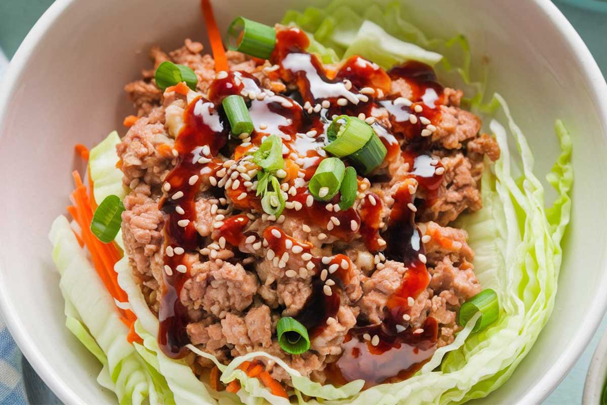 Bowl of egg roll in a bowl with ground meat, cabbage, and carrots, topped with sesame seeds and green onions.