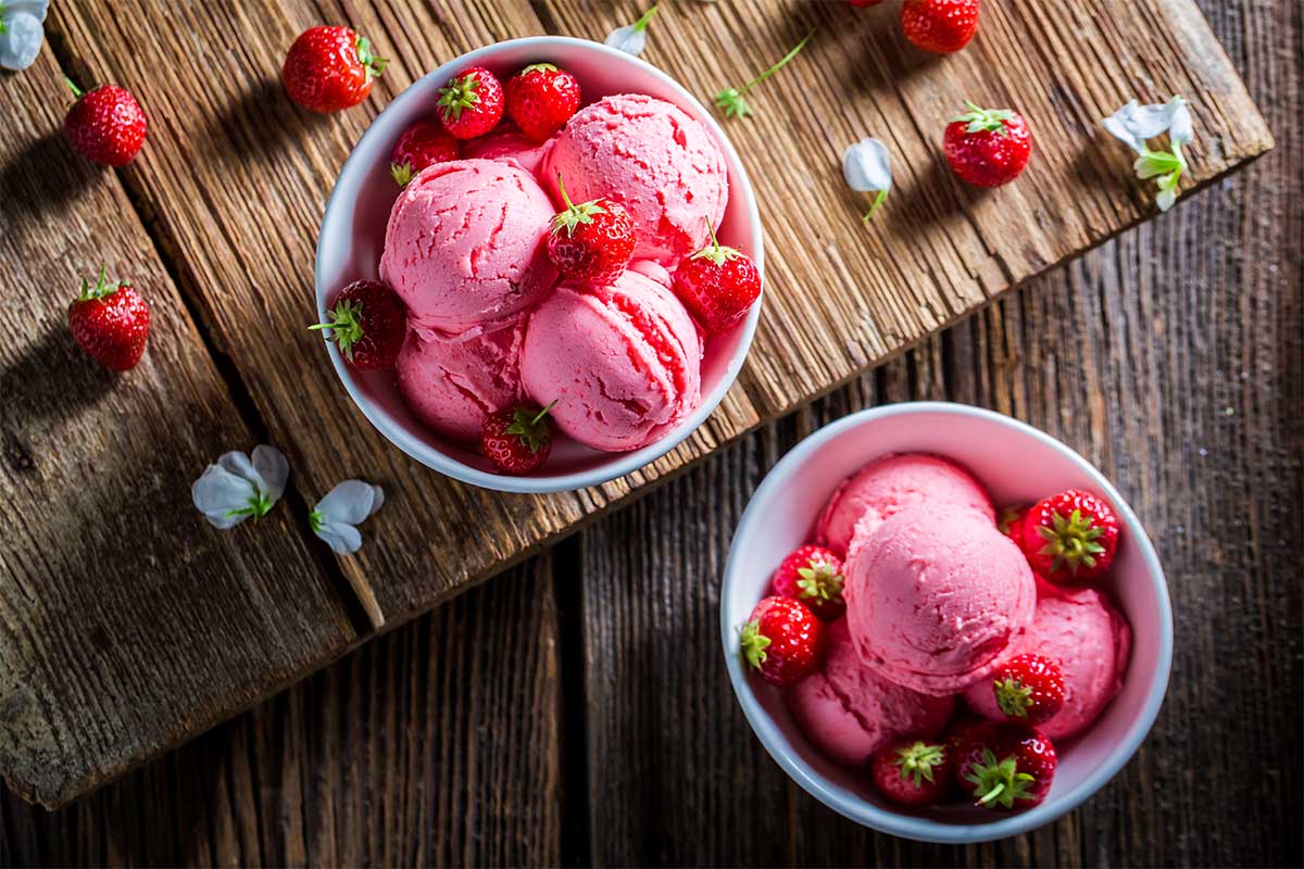 Homemade strawberry ice cream scooped in a bowl with fresh strawberries on the side.