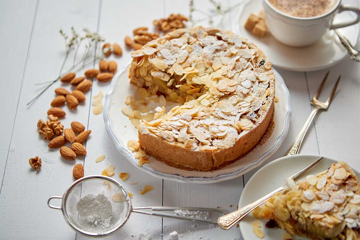 A freshly baked almond cake topped with flaked almonds and powdered sugar.