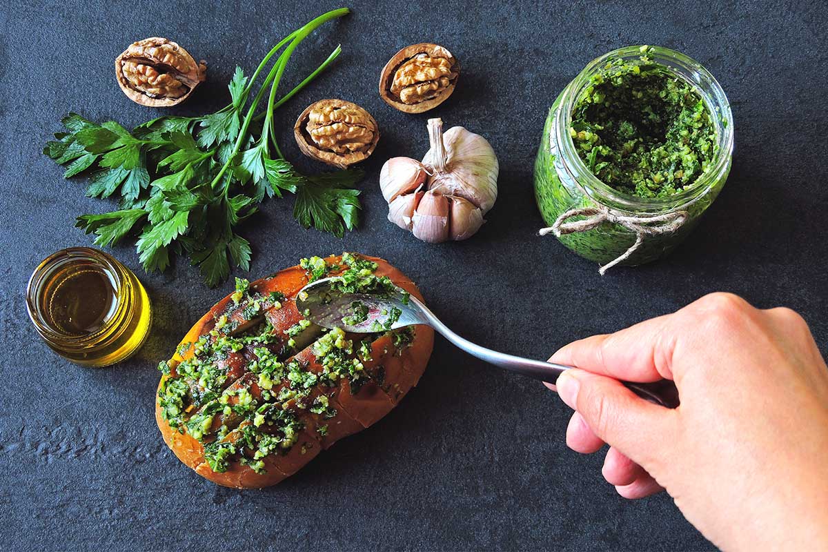 A vibrant jar of walnut pesto with fresh basil leaves and a spoon