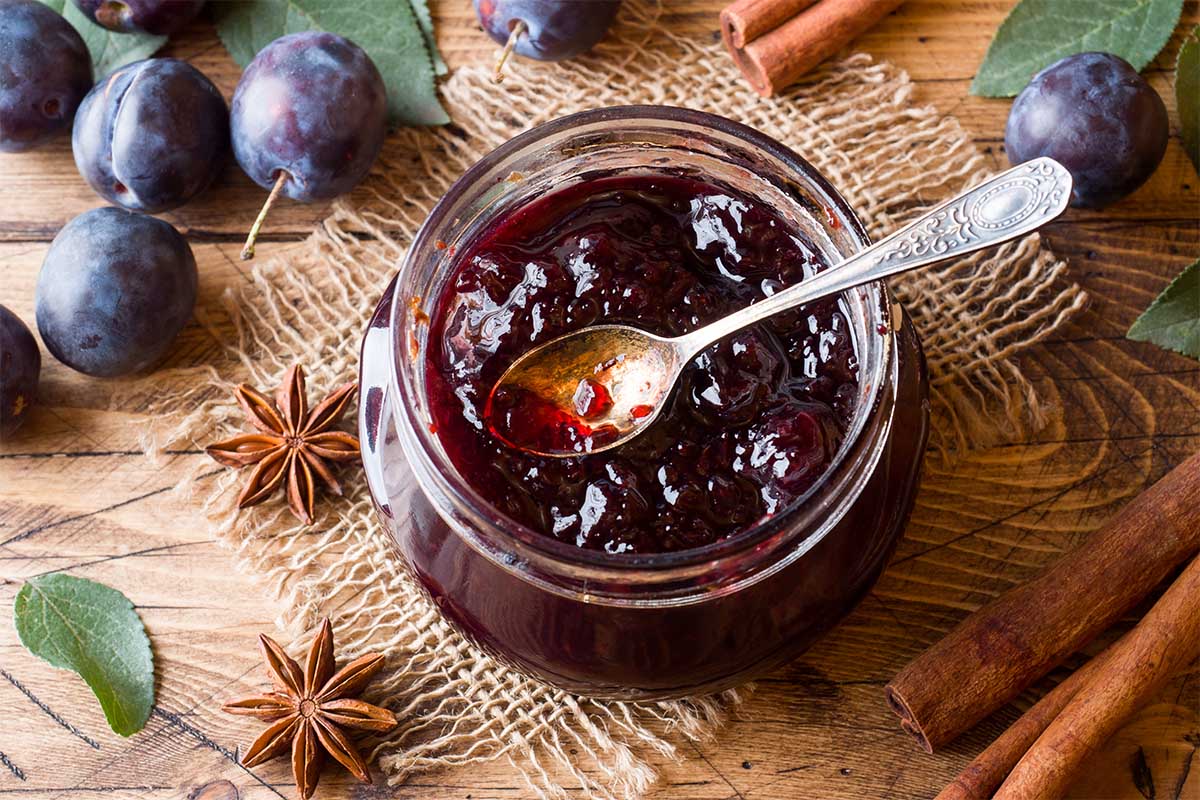 Jar of homemade plum jelly with fresh plums on a rustic kitchen table