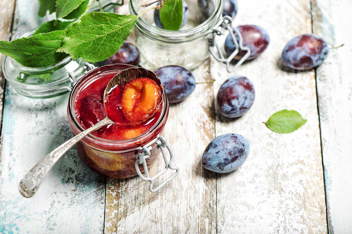 Jar of plum jam and jelly with fresh plums on a wooden table