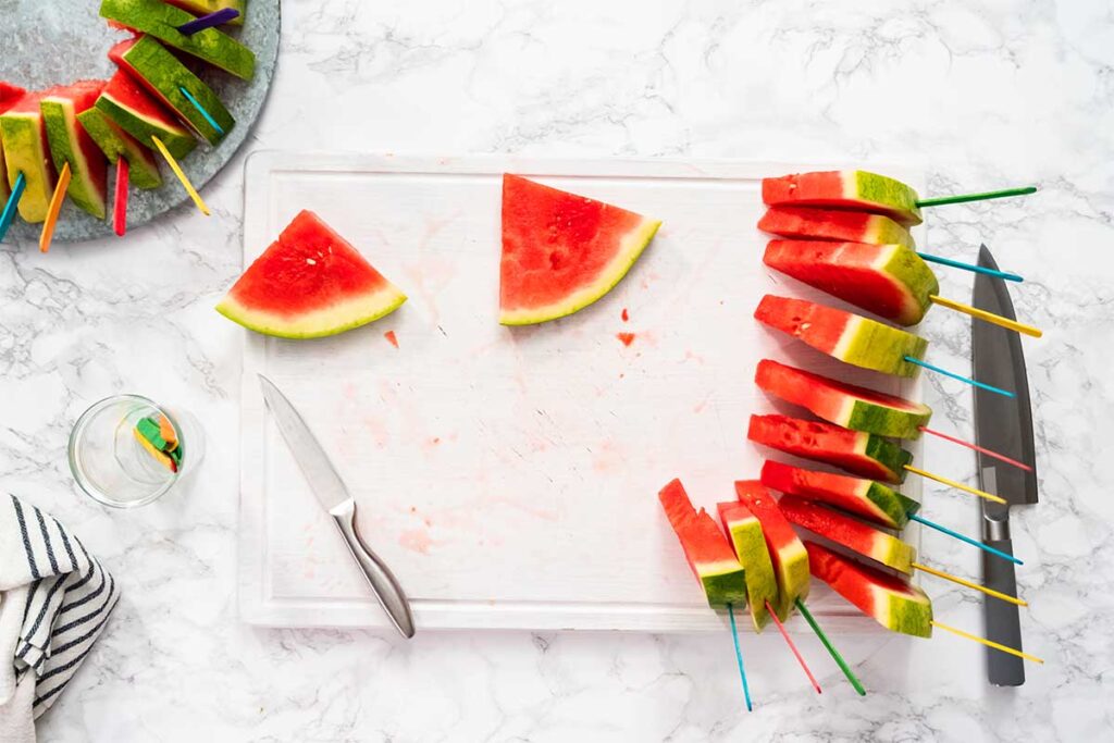 Slices of watermelon cut into popsicle shapes with sticks inserted